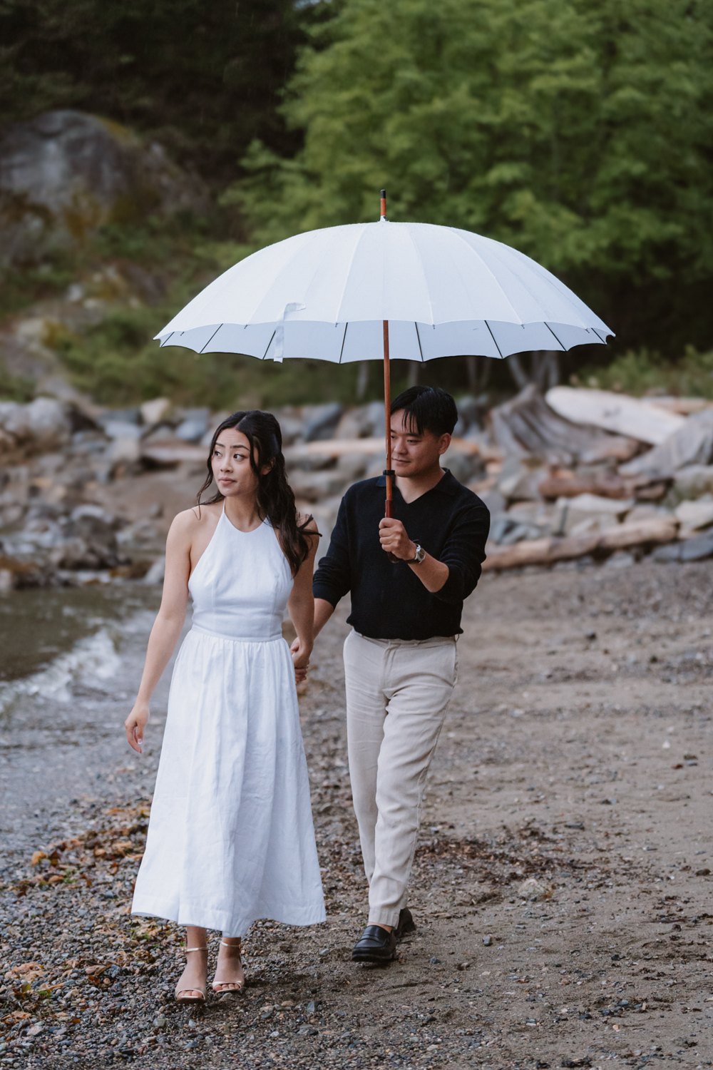 Aneeta and Christian under a clear umbrella on a driftwood beach