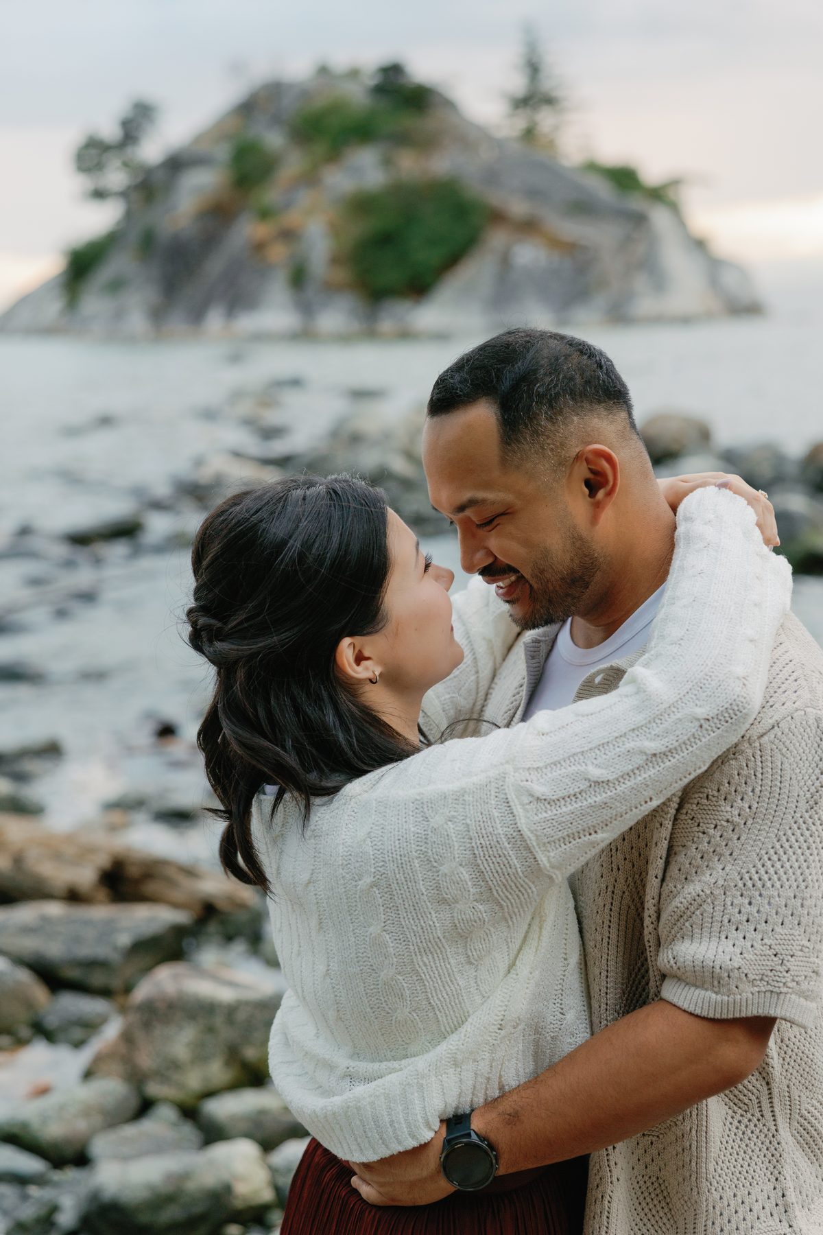 Couple holding each other on the rocks at the water's edge in West Vancouver