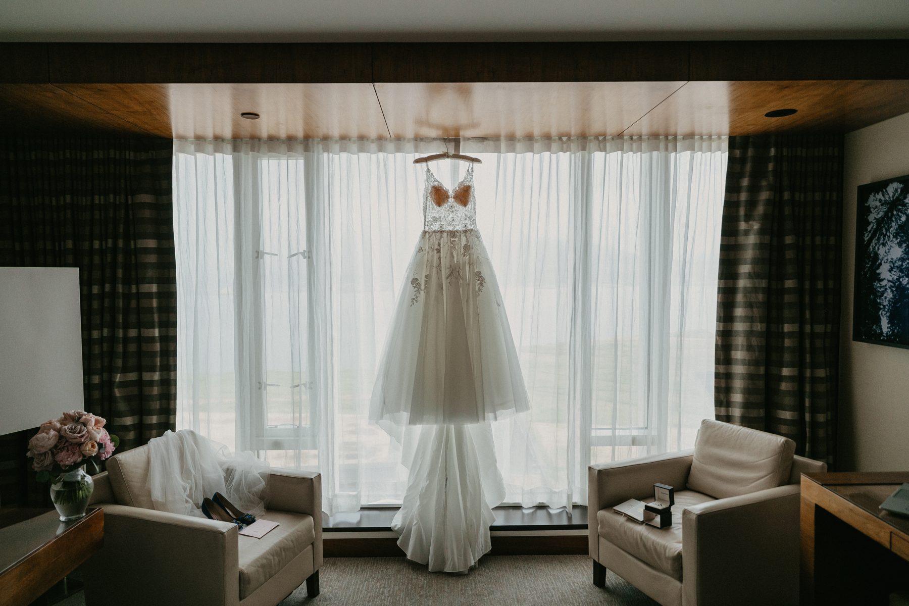 Wedding gown hanging in front of a hotel window with the city beyond