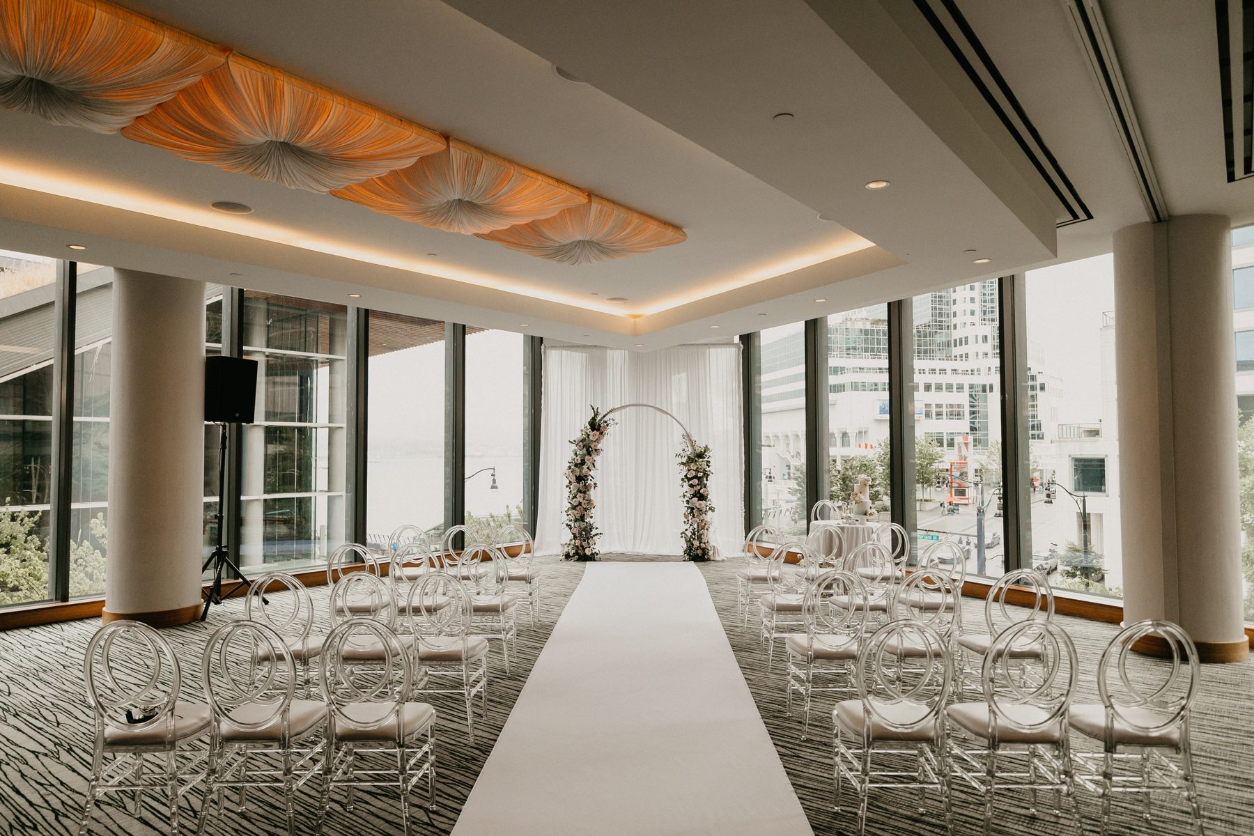 Rows of white chairs set for a ceremony in a ballroom with a glass wall overlooking downtown towers