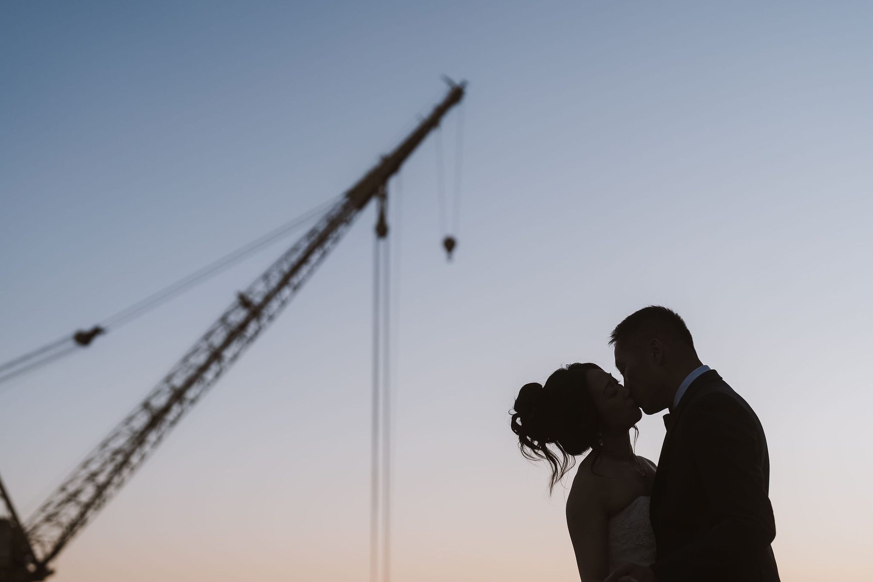 Silhouette of a couple kissing beneath a shipyard crane at dusk