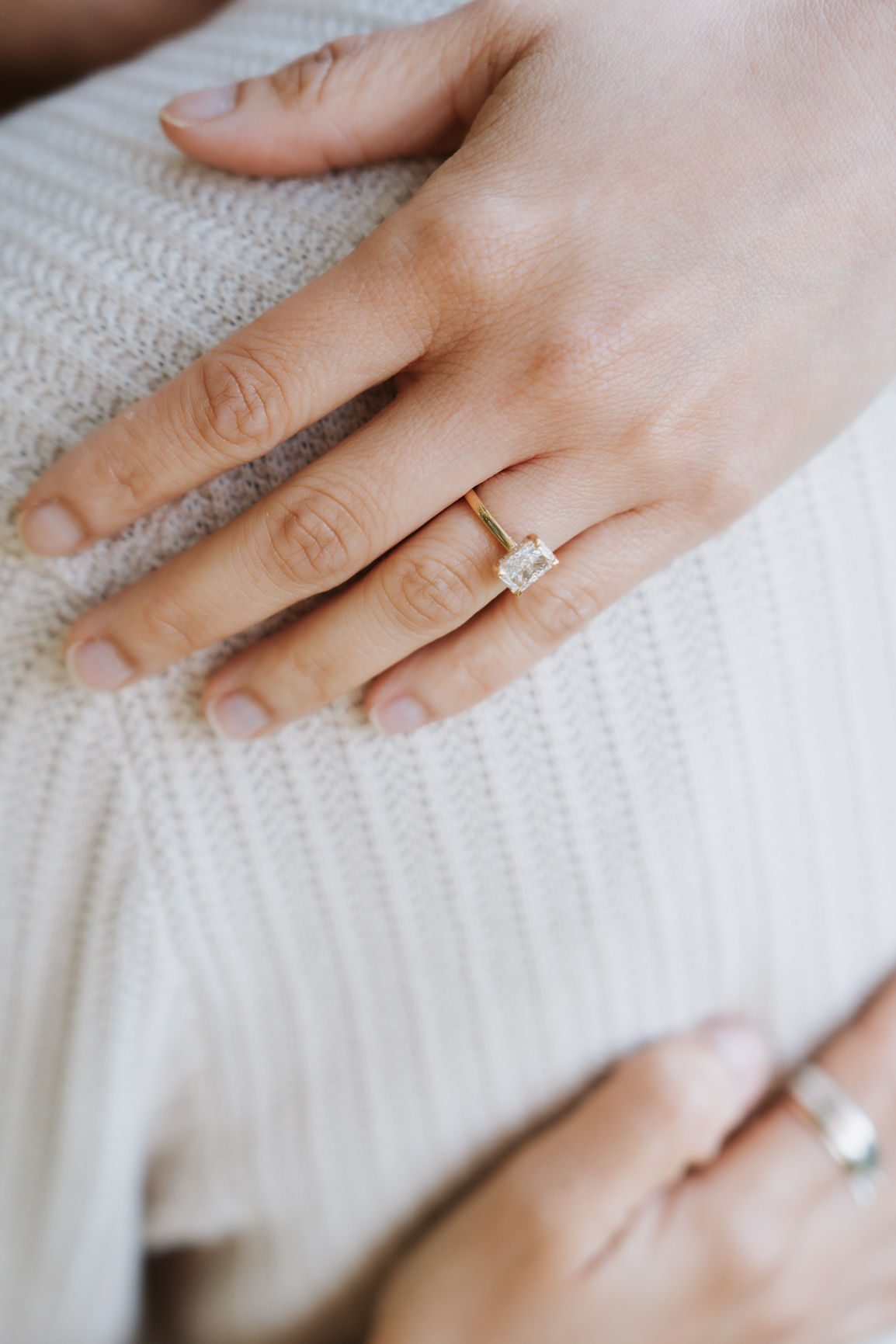 Close-up of an engagement ring on the hand resting against a knit sweater