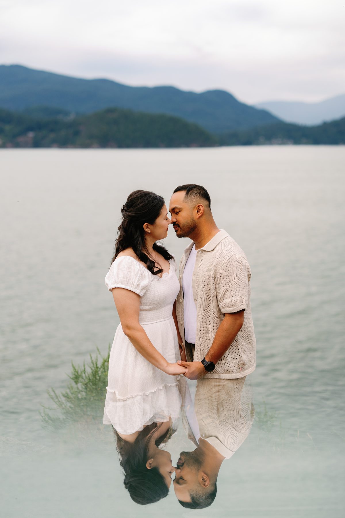 Couple standing forehead to forehead, mirrored in the still water at their feet